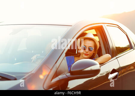 Smiling woman driving a car at sunset. Travel concept Stock Photo