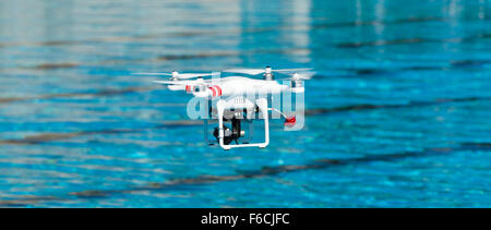 White drone quadcopter in flight with small camcorder. Stock Photo