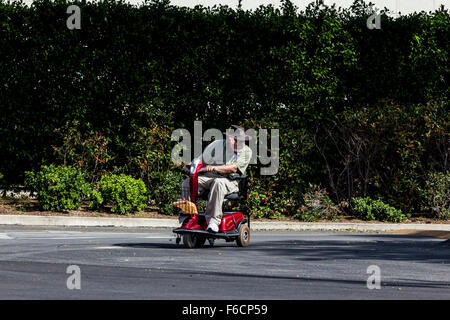 An elderly man riding his Rascal electric scooter leaning into the curve Stock Photo