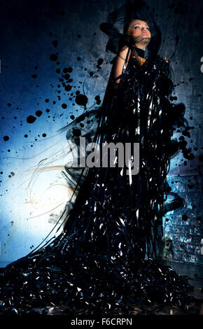 Young woman in black dress created from tape, smoke and spots. Dark dramatic colors. Stock Photo