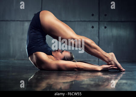 Strong woman bodybuilder stretching upside down in urban interior. Stock Photo