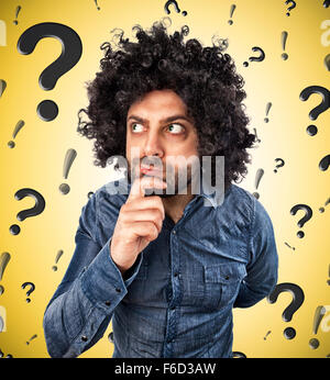 Young man thinks about something on background with question marks and exclamation marks Stock Photo