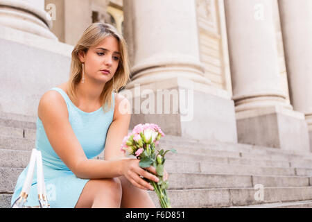 sad girl sitting on steps holding a bouquet of flowers Stock Photo