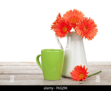 Orange gerbera flowers in pitcher and cup of drink on wooden table. Isolated on white background Stock Photo