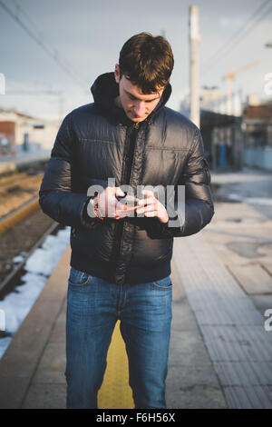 Knee figure of young handsome caucasian man using smartphone in the city, looking downward and tapping the screen - technology, Stock Photo