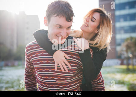 A couple of young lovers embraced, smiling and having fun in the city. He is looking downward and she is looking at him - love, Stock Photo