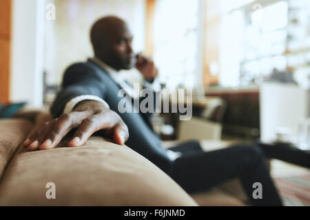 African businessman sitting in lounge area at hotel reception talking on mobile phone, focus on hand. Stock Photo