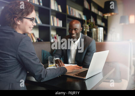 Young businesswoman showing presentation on laptop to her business partner. Happy executives in a meeting at restaurant Stock Photo