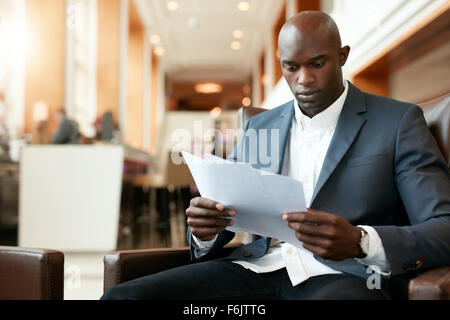 Portrait of young african businessman sitting at hotel lobby reading documents. business executive going through paperwork. Stock Photo