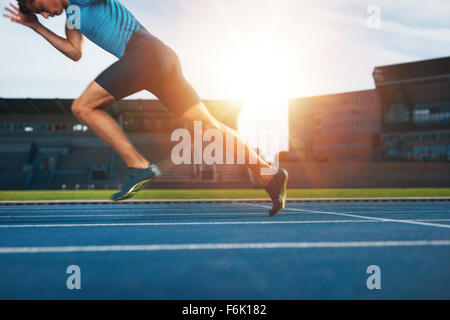 Shot of young male athlete launching off the start line in a race. Runner running on racetrack in athletics stadium. Stock Photo