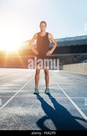 Full length shot of professional male athlete standing with his hands on hips looking confidently at camera. Sprinter on race tr Stock Photo