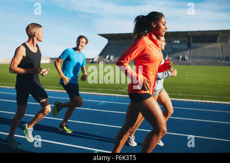 Fit men and women running on a race track. Multiracial athletes practicing on race track in stadium. Stock Photo