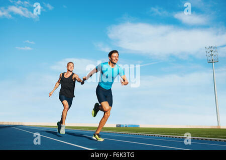 Shot of professional male athletes passing over the baton while running on the track. Athletes practicing relay race on racetrac Stock Photo