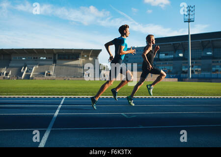 Two young men running on race track. Male professional athletes running on athletics race track. Stock Photo