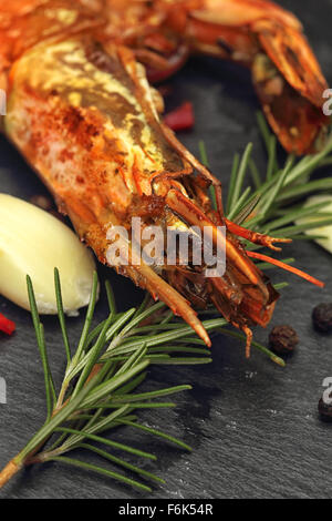 Grilled whole Giant Prawn with rosemary, garlic and red chili on a black slate background. Stock Photo