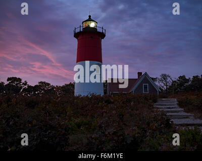 Nauset Light, a landmark red and white lighthouse at Nauset Light Beach in Eastham MA on Cape Cod Massachusetts USA, October 2015. Wide angle view with white beacon beam of light shining on dramatic pink and purple clouds in the blue hour just after sunset in autumn. The lighthouse has alternating red and white beacons. Stock Photo