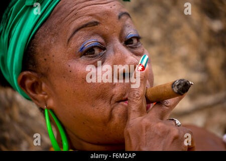 old heavily made Cuban woman with green hair bow smoking a Havana cigar, Cuban cigar with lacquered fingernails with Cuban Flag, Stock Photo