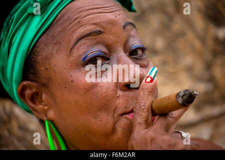 old heavily made Cuban woman with green hair bow smoking a Havana cigar, Cuban cigar with lacquered fingernails with Cuban Flag, Stock Photo