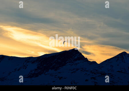 paraglider on a vibrant and bright dawn sky flying over majestic snow covered mountain top Stock Photo