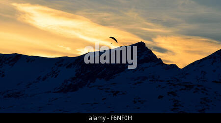 paraglider on a vibrant and bright dawn sky flying over majestic snow covered mountain top Stock Photo