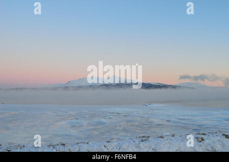 heavy eerie sea frost mist and fog over icy sea landscape with colorful dawn sky and snowy mountain Stock Photo