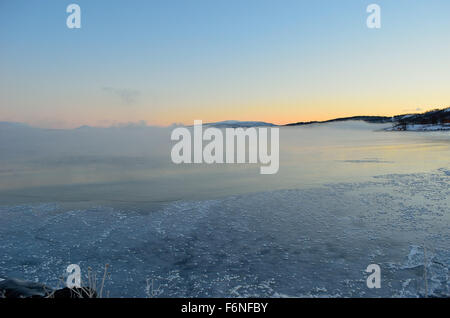 beautiful thick ice fog over cold fjord water with colorful sunset sky Stock Photo