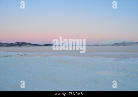 thick sea ice with cold ice frost fog and mist over water with pink colored dawn sky and snow