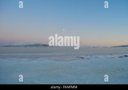 thick sea ice with cold ice frost fog and mist over water with pink colored dawn sky and snow Stock Photo