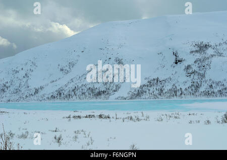 vibrant clear blue ice under mountain in winter landscape Stock Photo