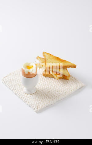 soft boiled egg in egg cup and crispy toasts on white table mat Stock Photo