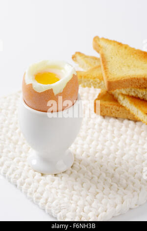 close up of soft boiled egg in egg cup and crispy toasts on white table mat Stock Photo