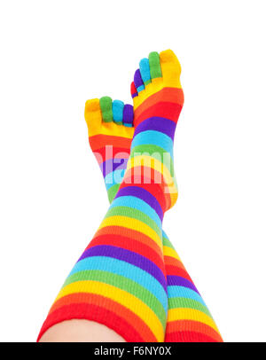 Female feet and legs in colorful striped rainbow socks raised up and relax. Isolated on white background Stock Photo