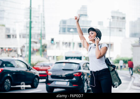 Knee figure of young handsome caucasian brown straight hair woman asking for a taxi raising her arms while talking smartphone, overlooking right, smiling - technology, communication, transport concept Stock Photo