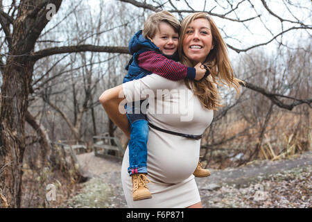 Happy child holding belly of pregnant woman in forest Stock Photo