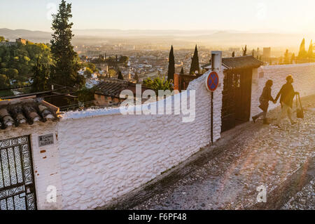 Couple walking at sunset through the alleys of the Moorish Albaicin quarter with Granada overview in background. Granada, Spain Stock Photo