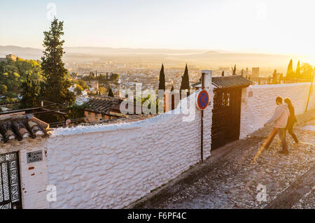 Couple walking at sunset through the alleys of the Moorish Albaicin quarter with Granada overview in background. Granada, Spain Stock Photo