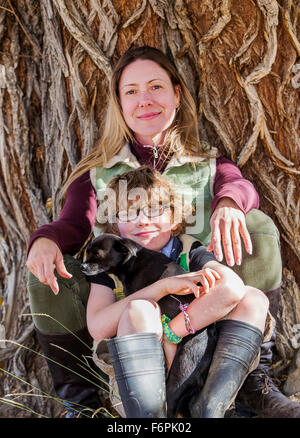Attractive mother and young son pose with pet dogs for photographs by tree on ranch Stock Photo