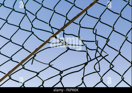 Torn hole in a wire mesh, hurricane, or cyclone steel fence Stock Photo