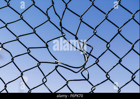 Torn hole in a wire mesh, hurricane, or cyclone steel fence Stock Photo