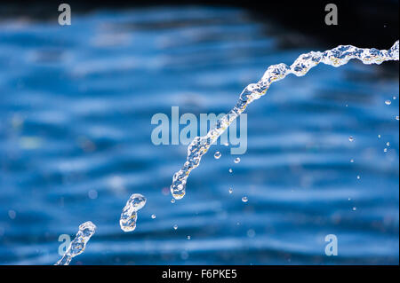 Abstract close-up of illuminated water stream and droplets falling in arc against blurred blue background. Stock Photo