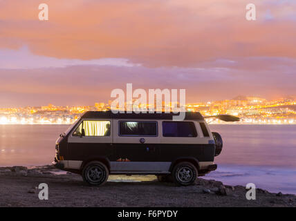 VW camper van parked on beach with city lights in background Stock Photo