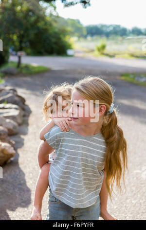 Caucasian girl carrying toddler brother piggyback Stock Photo