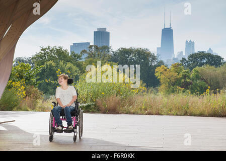 Paraplegic woman sitting in wheelchair under city skyline Stock Photo