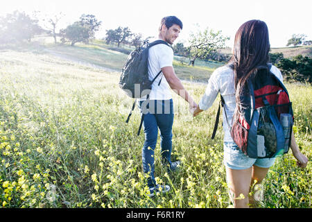 Couple carrying backpacks in field Stock Photo
