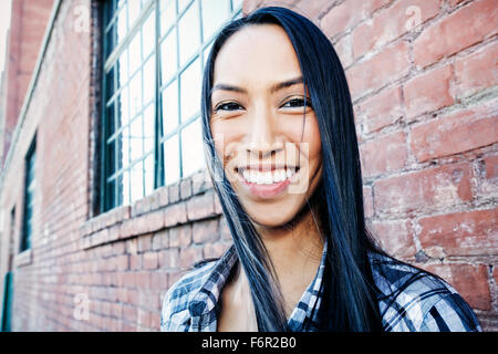 Mixed race woman smiling at brick wall Stock Photo