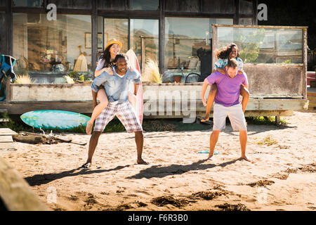 Men carrying girlfriends piggyback in sand Stock Photo