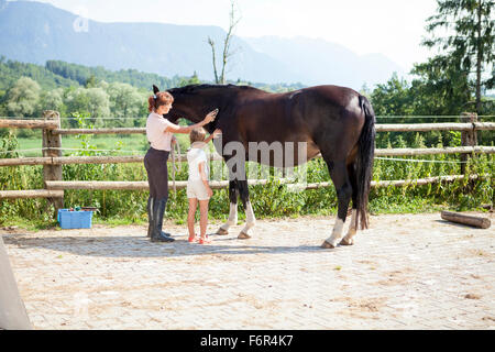Woman and girl grooming horse outdoors Stock Photo