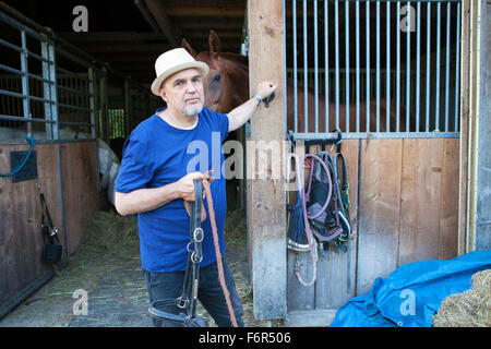 Senior man in front of stable holding horse's bridle Stock Photo