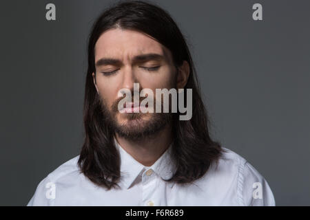 Portrait of a man with beard and long hair standing with closed eyes over gray background Stock Photo