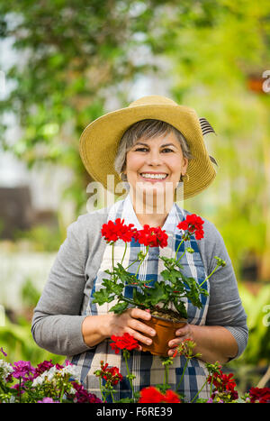 Mature woman in a greenhouse holding flowers Stock Photo